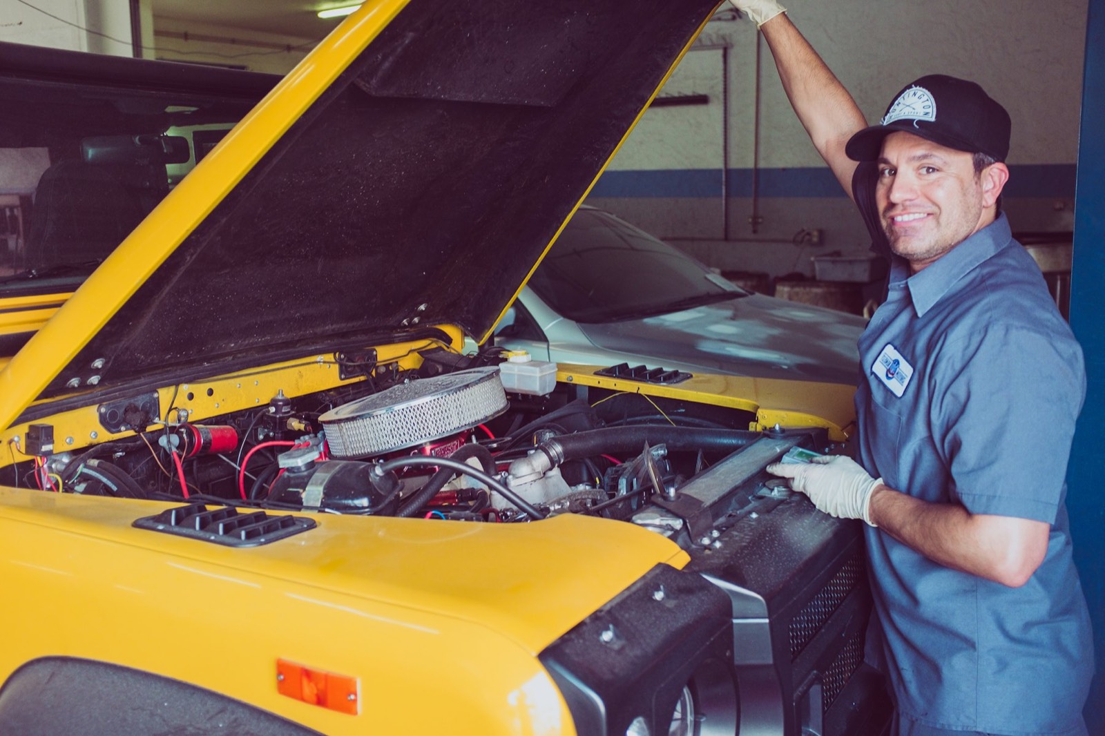 A smiling mechanic working under the hood of a car