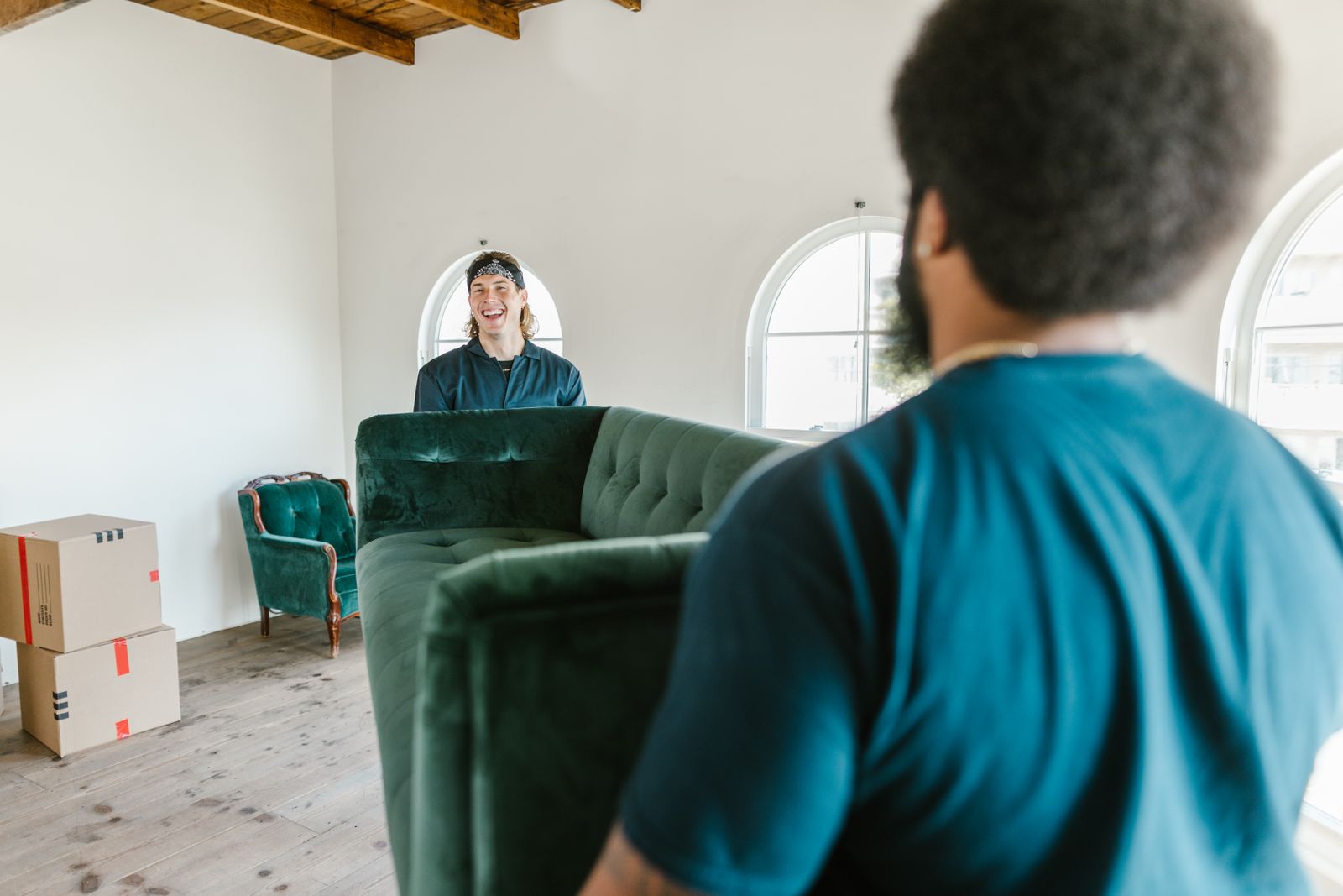 Two movers carrying a green couch through a bright, empty room