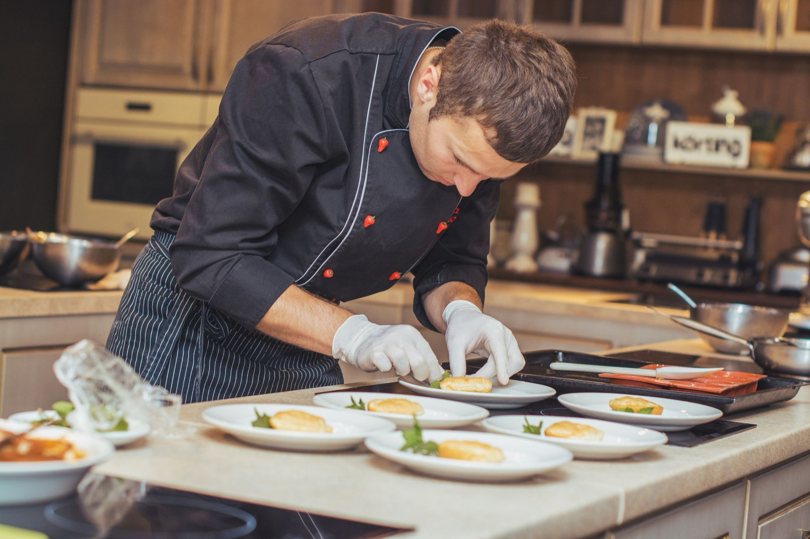 A chef plating a row of dishes in a restaurant kitchen