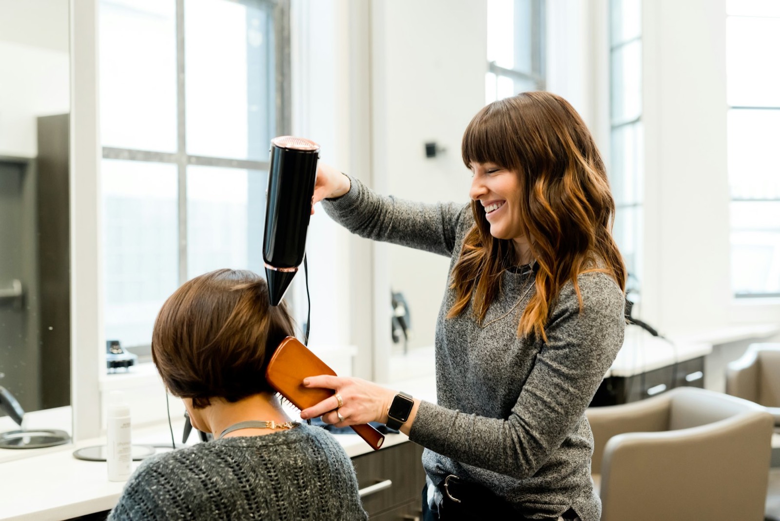 A smiling stylist blow-drying a client's hair
