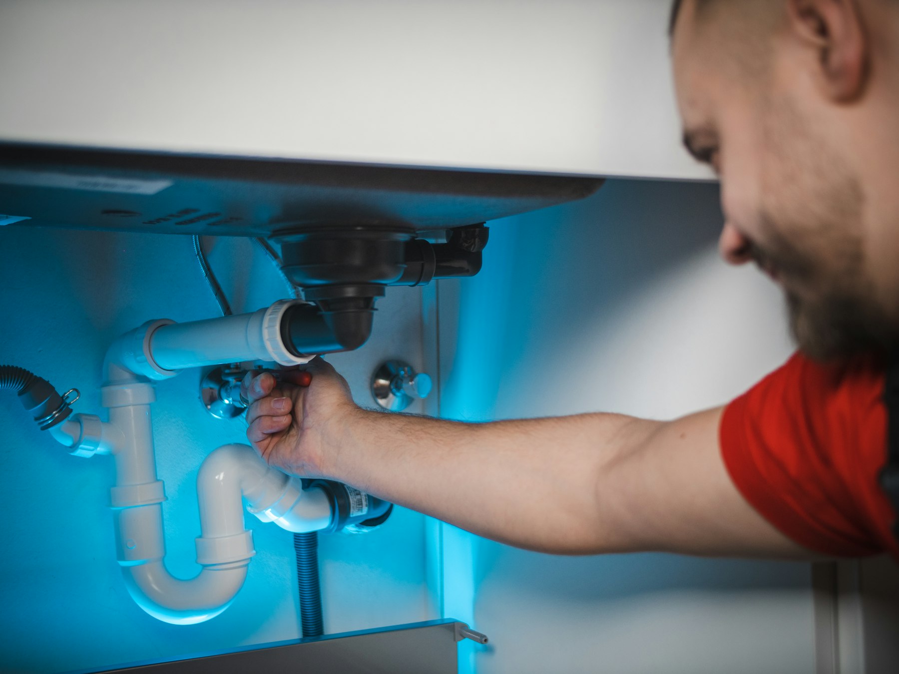 A smiling plumber fixing the pipes under a sink